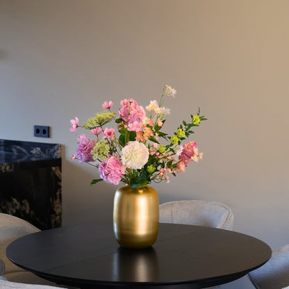 Kunstbloemen boeket met zijden bloemen in wit en roze tinten in een gouden vaas, gepresenteerd op een eettafel