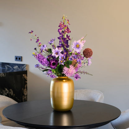 Kunstbloemen boeket met zijden bloemen in prachtige paarse tinten, in een gouden vaas, gepresenteerd op een eettafel