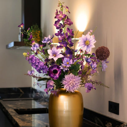 Kunstbloemen boeket met zijden bloemen in prachtige paarse tinten, in een gouden vaas, gepresenteerd in een keuken