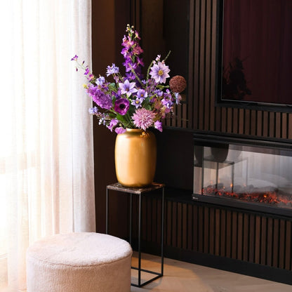 Kunstbloemen boeket met zijden bloemen in prachtige paarse tinten, in een gouden vaas, gepresenteerd in een woonkamer