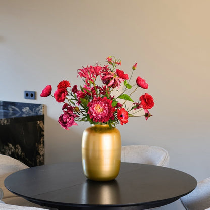 Prachtig kunstbloemen boeket met zijden bloemen in rood en roze tinten in een gouden vaas, gepresenteerd op een eettafel