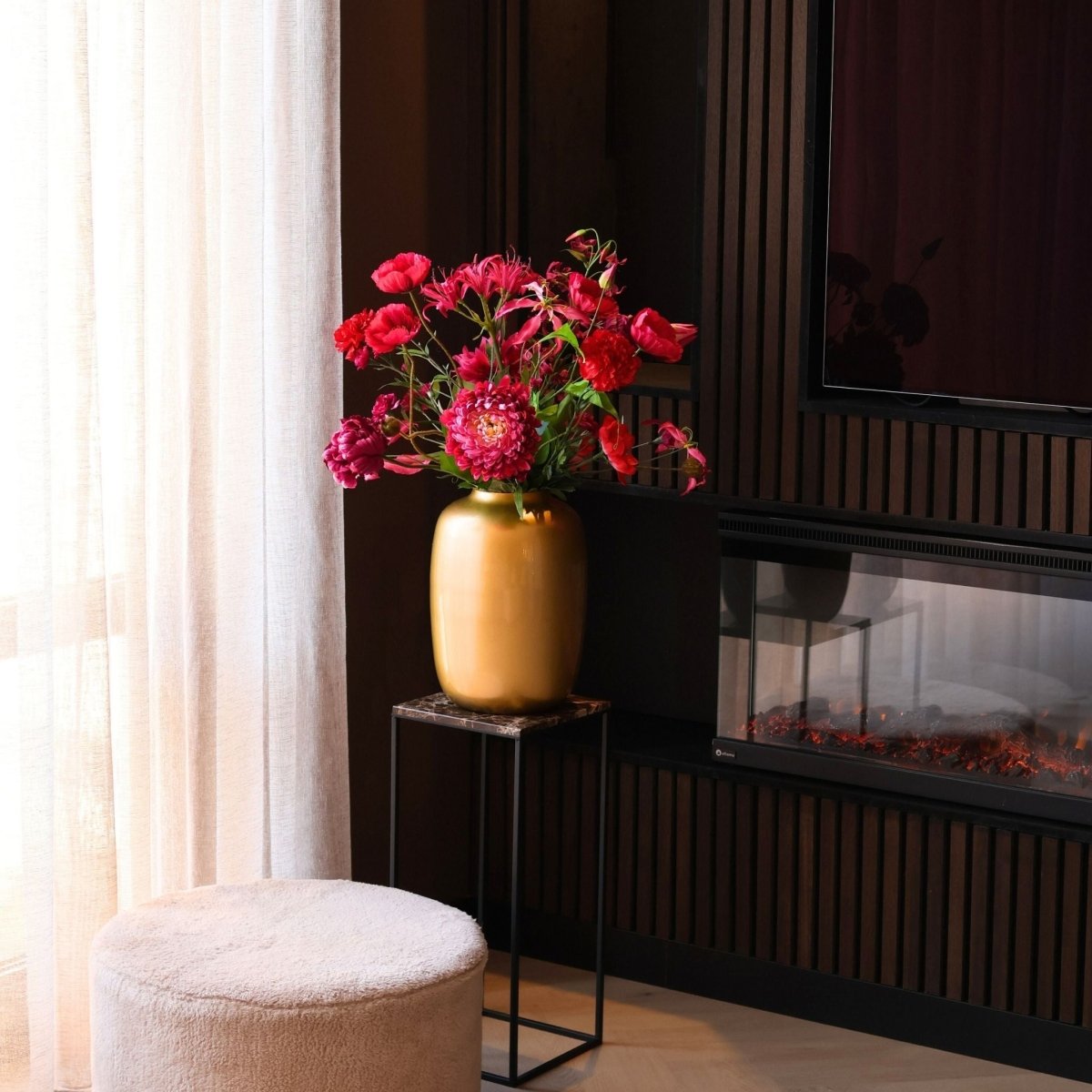 Prachtig kunstbloemen boeket met zijden bloemen in rood en roze tinten in een gouden vaas, gepresenteerd in een woonkamer